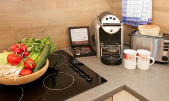 A modern kitchenette with fresh vegetables in a bowl, a coffee machine, and a toaster. There are also two white cups available.