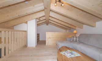 A modern attic room with a wooden ceiling and a bright sofa. The space is cozy and well-lit, perfect for relaxation.