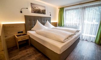 A modern bedroom with a cozy double bed and two large pillows. Large windows let in plenty of light and offer a view outside.