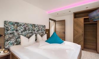 A modern bedroom with a cozy double bed and colorful pillows. The walls are light and the furniture is made of wood, creating a pleasant atmosphere.