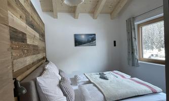 A cozy bedroom with wooden decor and a large window. The room is bright and inviting, perfect for relaxation.