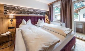 A cozy hotel room with two single beds and a modern decor. A large window view shows the surrounding landscape.