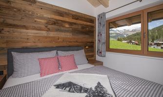 A cozy bedroom with wooden paneling and a large window. Outside, a beautiful mountain landscape can be seen.