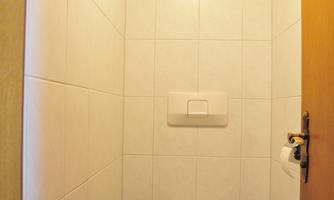 A small toilet with white tiles and a wooden ceiling. The space is simply and functionally designed.