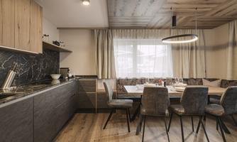 A modern kitchen with a wooden ceiling and elegant furniture. A large table with chairs invites you to dine.