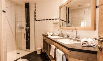 A modern bathroom with a shower and a large mirror. The washing area is made of wood with two sinks and fresh towels.
