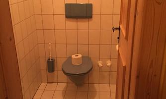 A small bathroom with a toilet and a shelf. The walls are tiled, and there is a wooden frame.
