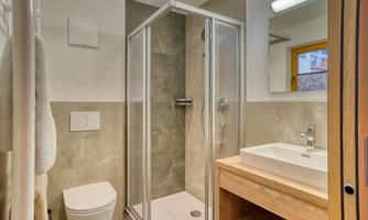 A modern bathroom with a shower and a wooden washbasin. The walls are in neutral colors and there is plenty of light.