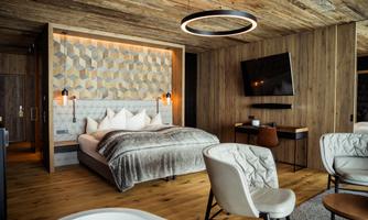 A modern bedroom with wooden paneling and geometric patterns on the wall. It features a large bed, comfortable armchairs, and a television.