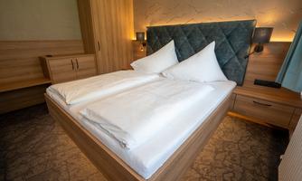 A modern bedroom with a large double bed and two pillows. The walls are painted in light tones and there are wooden furnishings.