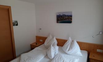 A simple bedroom with two beds and wooden furniture. A picture of a landscape hangs on the wall.