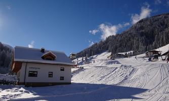 A winter landscape with snow-covered hills and a cozy cabin. The sky is clear and blue, perfect for a skiing trip.