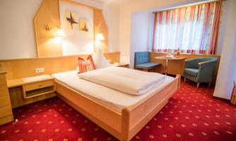 A cozy hotel room with a large bed and a red carpet. There is a seating area with a clean window and soft lighting.