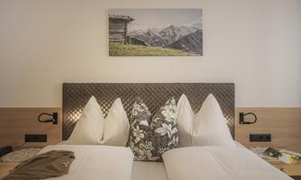 A cozy bedroom with two beds and decorative pillows. A photo of mountain landscapes hangs on the wall.