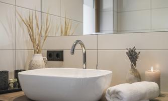 A modern bathroom with an elegant sink and a wooden shelf. Decorative elements like dried plants and a candle create a relaxed atmosphere.