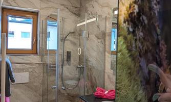 A modern bathroom with a glass shower and elegant marble walls. Towels in various colors can be seen and a window that lets in natural light.