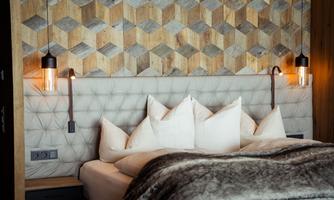 A cozy bedroom with a padded headboard and plenty of pillows. The walls are decorated with a modern wood design.