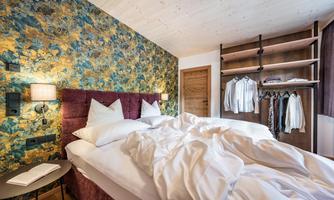 A cozy bedroom with a modern design. The bed is unmade, and there is an open wardrobe with clothes.