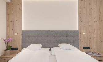 A modern bedroom with a padded headboard and soft lighting. A blooming orchid is on the nightstand.
