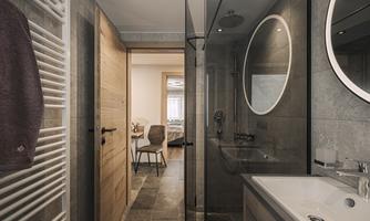 A modern bathroom with a shower and a large mirror. The room is stylishly designed with gray tiles and a wooden ceiling.