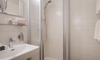A modern bathroom with a shower cabin and a sink. The walls are brightly tiled and there is a towel holder.