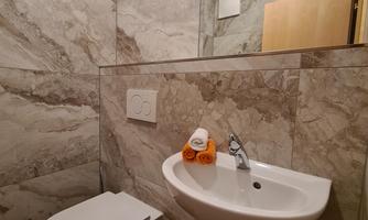 A modern bathroom with gray marble and a white toilet. A small sink with soap and a mirror are also visible.