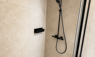 A modern shower area with an elegant tiled surface. The black shower with rain showerhead and handheld shower provides a pleasant shower experience.
