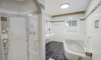 A modern bathroom with a shower and a bathtub. The walls are tiled in light colors and the floor is dark gray.