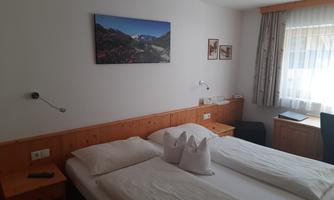 A cozy bedroom with two beds and wooden details. A picture of a mountain landscape hangs on the wall.