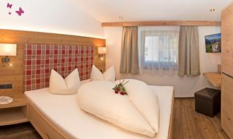 A cozy bedroom with wooden decor and a large, heart-shaped pillow. Fresh strawberries are lying on the bed as a nice surprise.