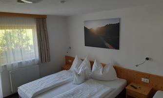 A cozy hotel room with two beds and white pillows. A picture of a mountain landscape in the sunlight hangs on the wall.