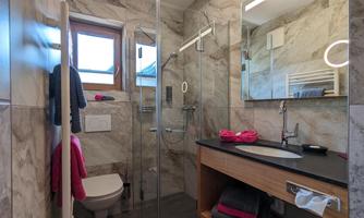 A modern bathroom with a glass shower and marble walls. The room is bright and has practical shelving.