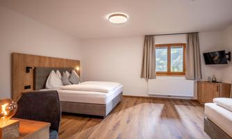 A modern bedroom with a double bed and a large window. The room is cozily furnished with wooden details and a television.