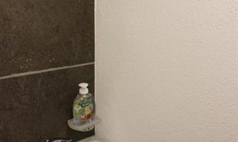 A small sink on a wall with a dark tile. There is a bar of soap on the shelf.