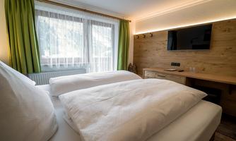 A modern bedroom with a large bed and two pillows. There is a television on the wall and there are large windows with green curtains.