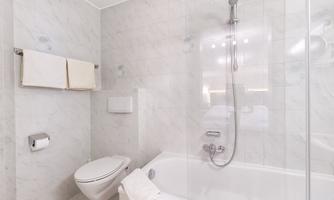 A modern bathroom with a bathtub and a shower. The walls are tiled with white tiles and there are fresh towels.