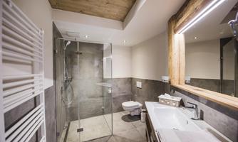A modern bathroom with a shower and a sink. The walls are in neutral colors and a wooden beam provides a warm accent.