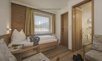 A cozy hotel room with two beds and a large window. The wood paneling and the chair create a warm atmosphere.