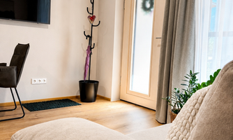 A modern living room with a comfortable sofa and a television on the wall. At the door stands a coat rack and a few plants adorn the room.