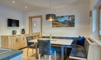 A modern kitchen with wood decor and a dining area. A landscape painting hangs on the wall and a TV is visible.