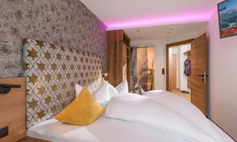 A modern bedroom with a large bed and stylish decoration. Soft, colored lighting creates a relaxing atmosphere.
