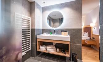A modern bathroom with an elegant vanity combination and a round mirror. The walls are painted in neutral tones, and there are towels and care products visible.