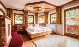A cozy bedroom with wooden paneling and large windows. The room is bright and inviting, with a large bed and a carpet.