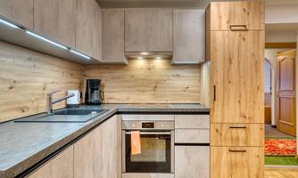 A modern kitchen with wooden and gray cabinets. The room is well-lit and contains essential appliances like a stove and a coffee machine.