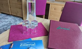 A table with a water carafe and two glasses. Next to it are brochures and a menu.