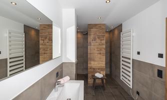 A modern bathroom with a large mirror and a stylish wooden accent. The walls are in neutral tones, and there is underfloor heating.
