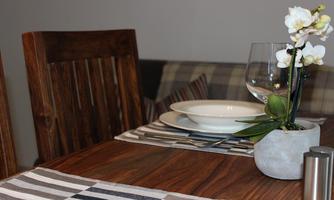 A stylish dining area with a wooden table, a white bowl, and a glass. Decorated with a small orchid in a modern pot.
