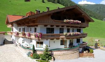 A beautiful country house with traditional architecture and colorful flowers on the balcony. The surroundings are filled with green meadows and mountains.