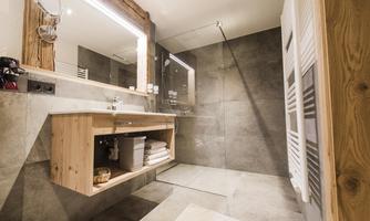 A modern bathroom with an elegant shower and a wooden washbasin. The walls are in neutral gray tones, creating a calm atmosphere.