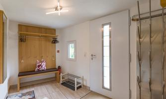 An inviting hallway with a shoe rack and coat stand. The wall is light-colored and there is a window that provides natural light.